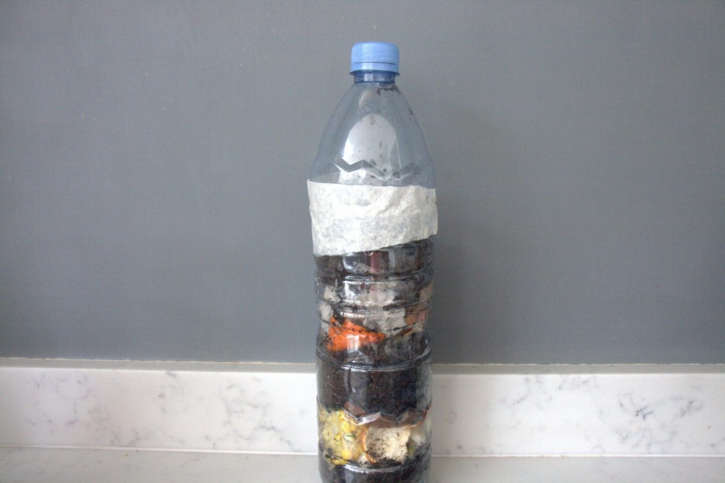 Large clear plastic bottle filled with compost material and taped shut